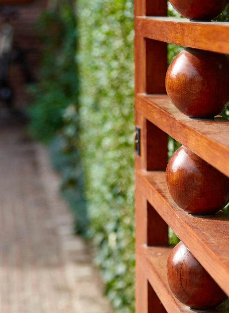Wooden garden gate with decorative round elements leading to a brick pathway surrounded by lush greenery