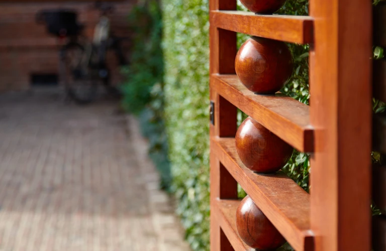 Wooden garden gate with decorative round elements leading to a brick pathway surrounded by lush greenery